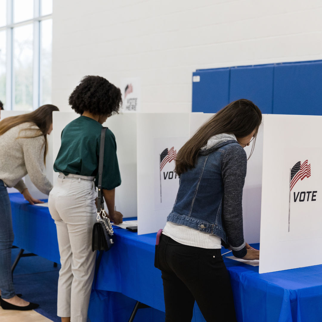 Women stand at a voting booth filling out their ballots.